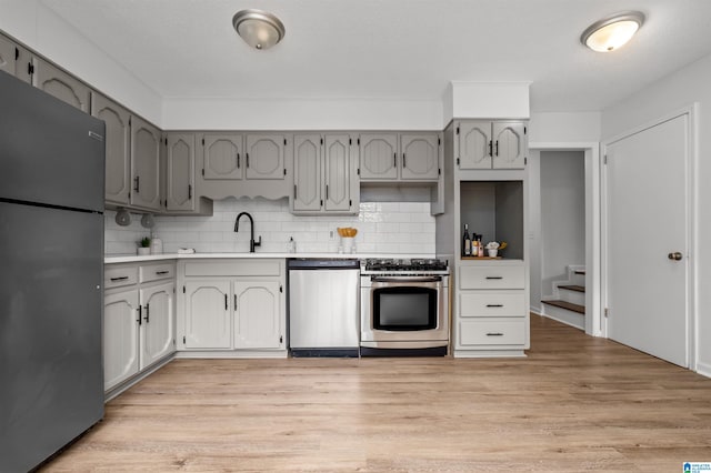 kitchen with light wood-type flooring, sink, decorative backsplash, stainless steel appliances, and gray cabinetry