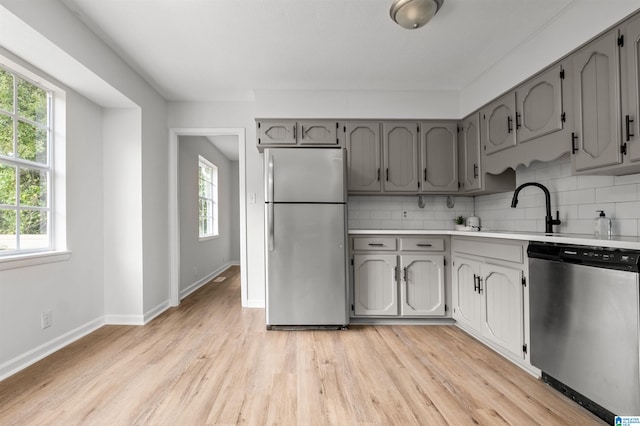 kitchen with gray cabinets, light hardwood / wood-style floors, sink, stainless steel appliances, and backsplash