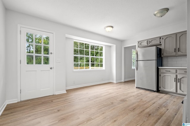 kitchen featuring gray cabinetry, light hardwood / wood-style floors, tasteful backsplash, and stainless steel refrigerator