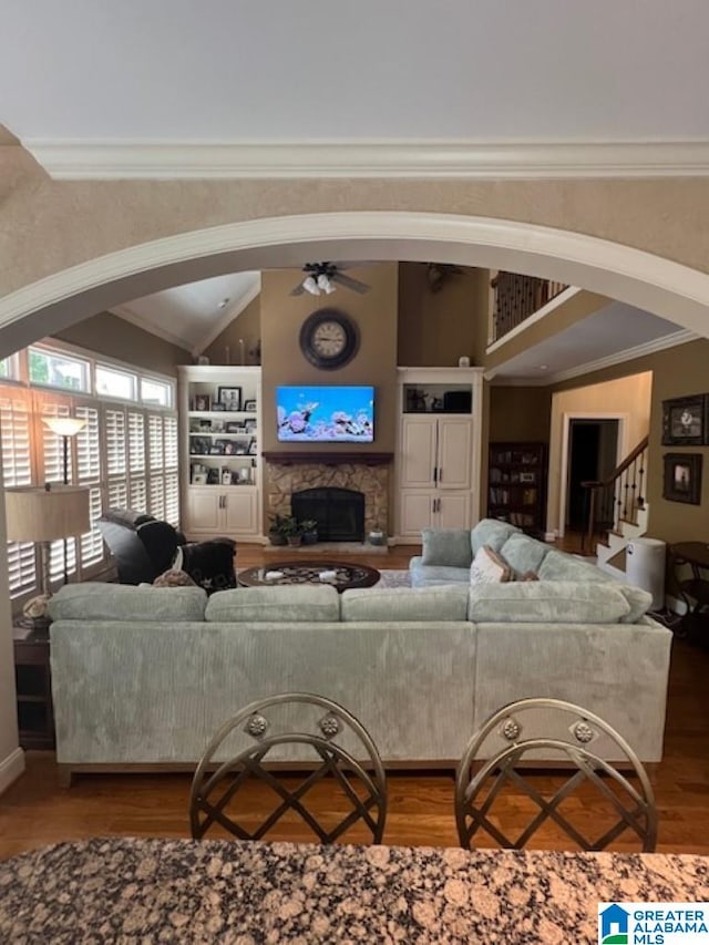 living room with wood-type flooring, a stone fireplace, ornamental molding, and ceiling fan