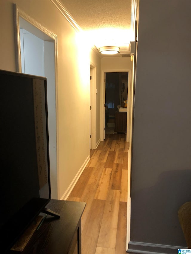 corridor featuring a textured ceiling, light wood-type flooring, and ornamental molding