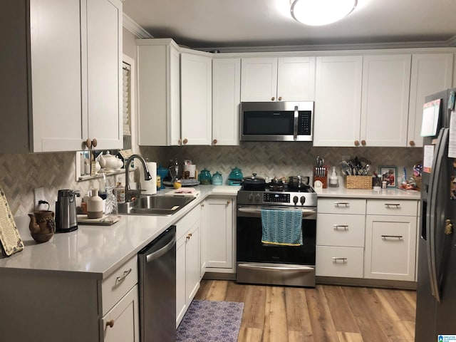 kitchen with appliances with stainless steel finishes, white cabinets, light wood-type flooring, crown molding, and sink