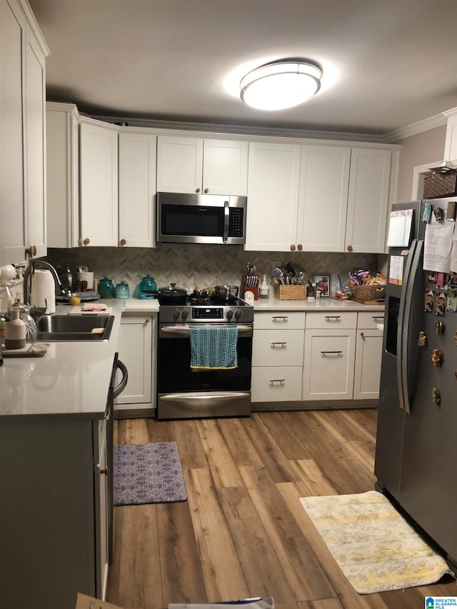 kitchen with light hardwood / wood-style floors, tasteful backsplash, sink, white cabinetry, and appliances with stainless steel finishes