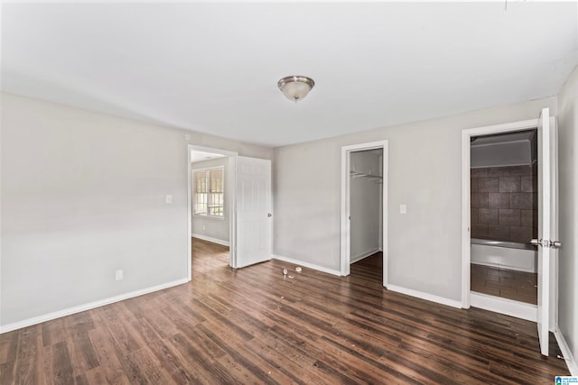 unfurnished bedroom with a closet, a walk in closet, and dark wood-type flooring