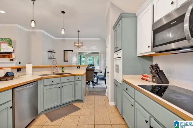 kitchen featuring pendant lighting, light tile patterned flooring, sink, ornamental molding, and stainless steel appliances