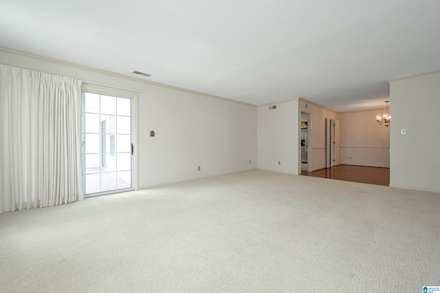 carpeted empty room with a textured ceiling, ornamental molding, and an inviting chandelier