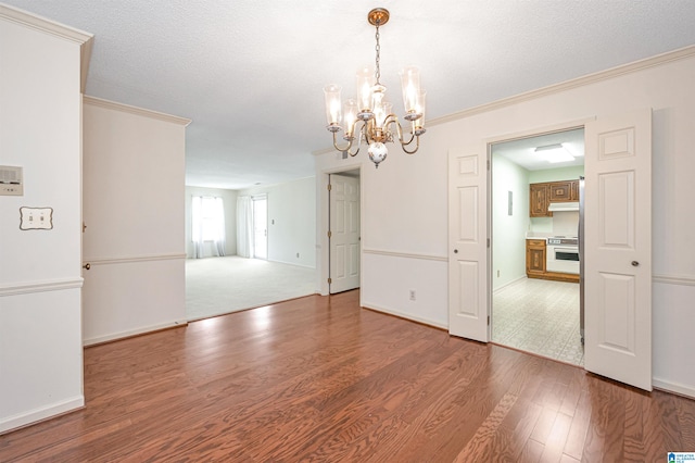 unfurnished dining area featuring a textured ceiling, ornamental molding, an inviting chandelier, and hardwood / wood-style flooring