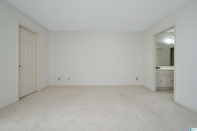 unfurnished bedroom with a textured ceiling, connected bathroom, and light carpet