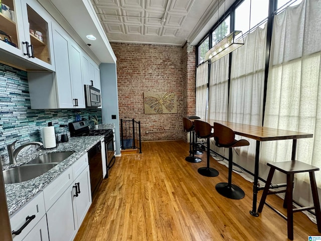 kitchen with light wood-type flooring, sink, white cabinets, light stone countertops, and brick wall