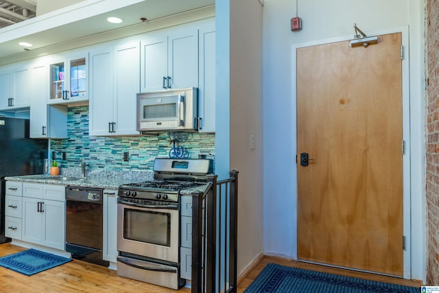 kitchen featuring appliances with stainless steel finishes, white cabinetry, tasteful backsplash, light stone countertops, and light wood-type flooring