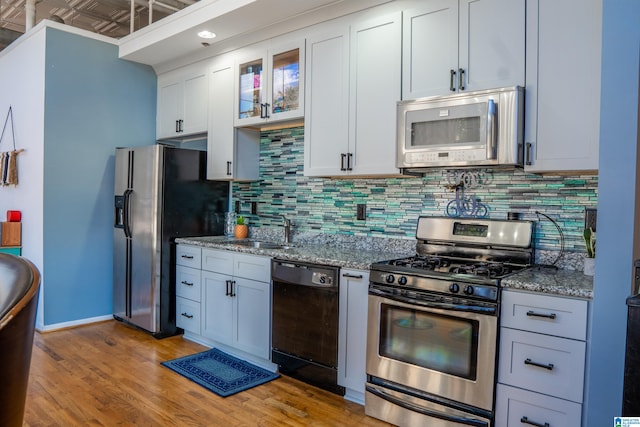 kitchen with stainless steel appliances, light wood-type flooring, sink, and stone counters