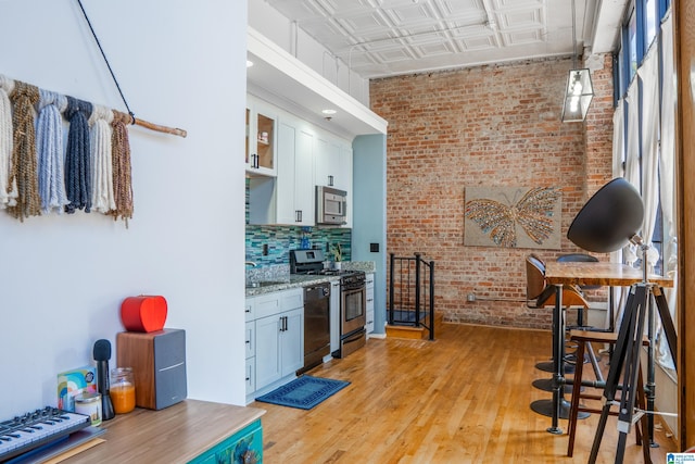 kitchen with light stone counters, light hardwood / wood-style floors, white cabinetry, appliances with stainless steel finishes, and brick wall