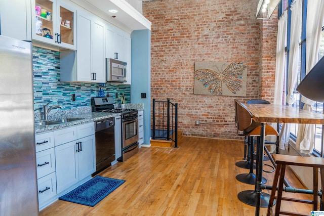 kitchen featuring light stone counters, white cabinets, brick wall, light hardwood / wood-style flooring, and black appliances