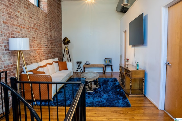 living room with brick wall, a high ceiling, and hardwood / wood-style flooring