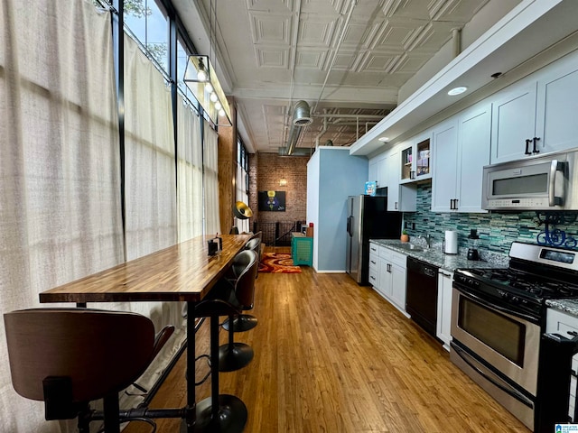 kitchen with white cabinets, appliances with stainless steel finishes, light wood-type flooring, and light stone countertops