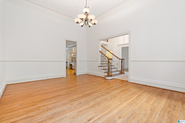 spare room with an inviting chandelier, light wood-type flooring, and ornamental molding