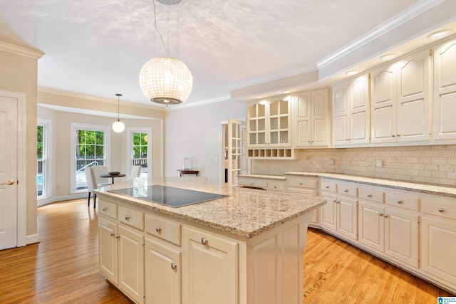 kitchen featuring light wood-type flooring, hanging light fixtures, backsplash, light stone countertops, and crown molding