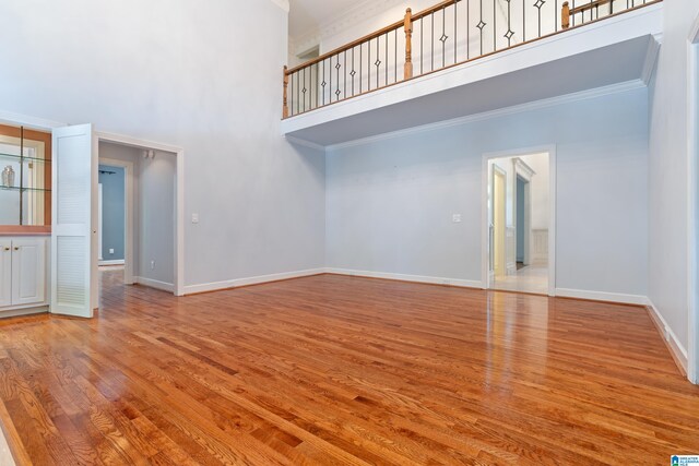 unfurnished living room with light hardwood / wood-style floors, crown molding, and a high ceiling