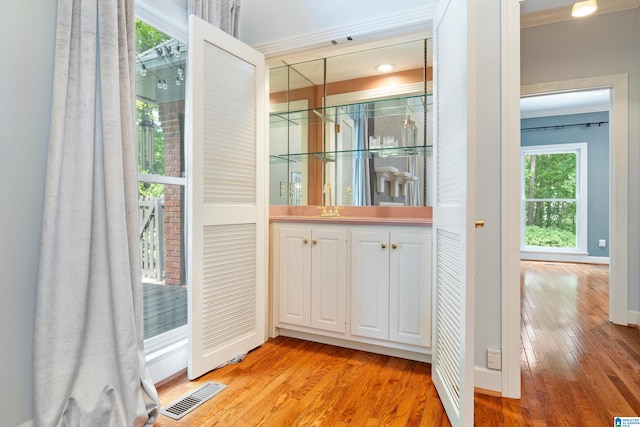 bar featuring crown molding, light hardwood / wood-style floors, and white cabinetry