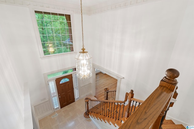 entryway featuring ornamental molding, an inviting chandelier, parquet flooring, and a high ceiling