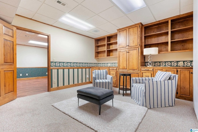 living area featuring a paneled ceiling, built in features, and light colored carpet