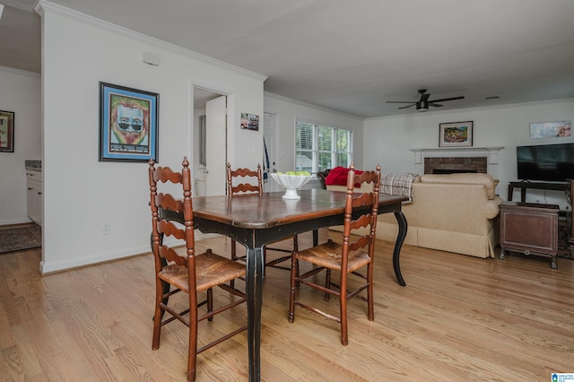 dining area with a brick fireplace, light wood-type flooring, ceiling fan, and ornamental molding