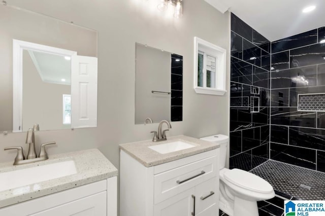 full bath with two vanities, a tile shower, toilet, and a sink