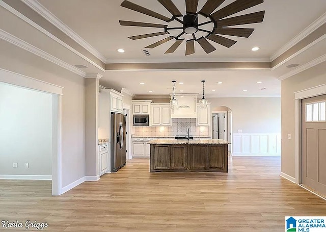 kitchen featuring pendant lighting, stainless steel appliances, a center island with sink, and crown molding