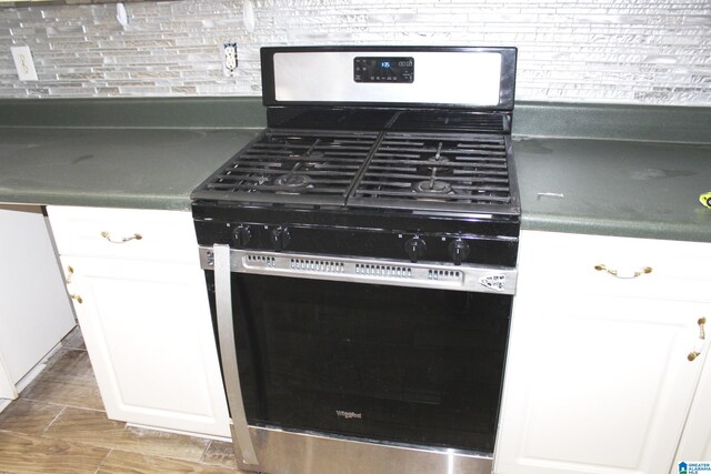 kitchen with stainless steel gas range oven, decorative backsplash, and white cabinetry