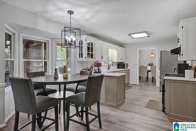 kitchen with range, white cabinets, exhaust hood, an inviting chandelier, and light hardwood / wood-style flooring