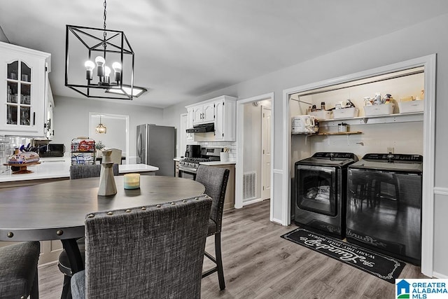 kitchen with white cabinets, stainless steel appliances, light hardwood / wood-style flooring, decorative light fixtures, and washer and clothes dryer