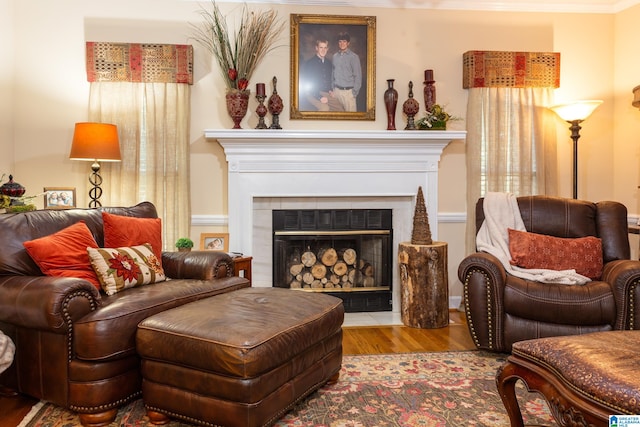 sitting room with light wood-type flooring, ornamental molding, and a tiled fireplace