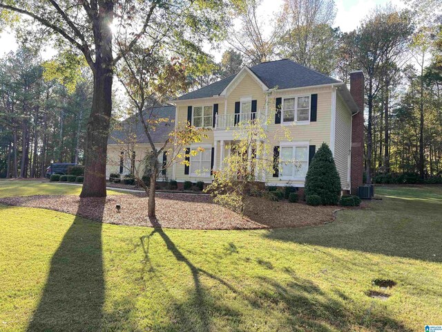 colonial inspired home with a front yard, a chimney, central AC unit, and a balcony
