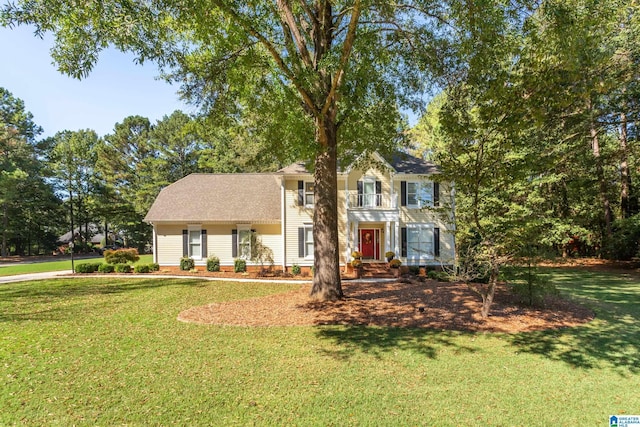 colonial inspired home with a front lawn, a shingled roof, and a balcony