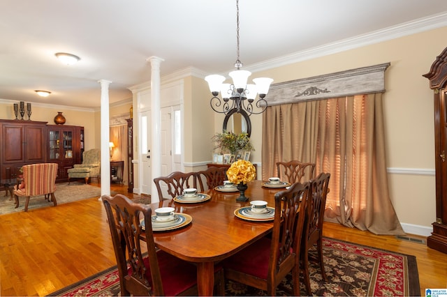 dining room featuring decorative columns, ornamental molding, an inviting chandelier, and light hardwood / wood-style flooring