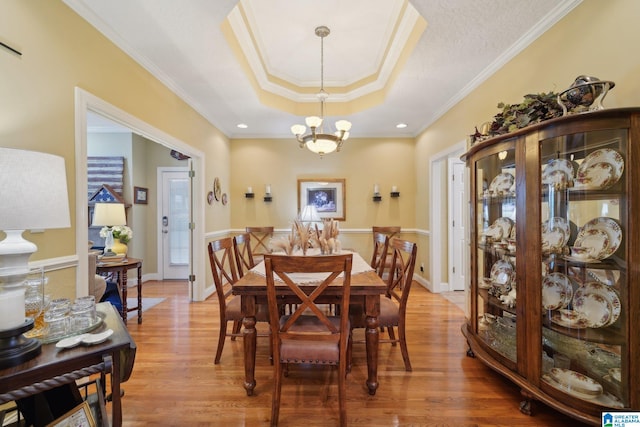 dining space with crown molding, hardwood / wood-style floors, a chandelier, and a raised ceiling