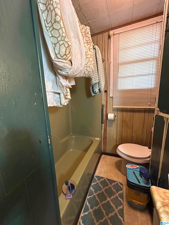 full bathroom featuring wood walls, shower / bathtub combination with curtain, tile patterned floors, vanity, and toilet