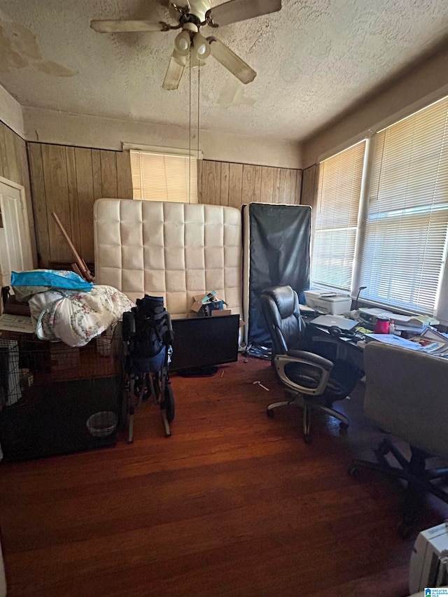 office space with ceiling fan, a textured ceiling, wooden walls, and dark hardwood / wood-style flooring