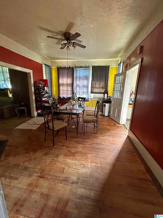 dining area with a textured ceiling, wood-type flooring, wood walls, and ceiling fan