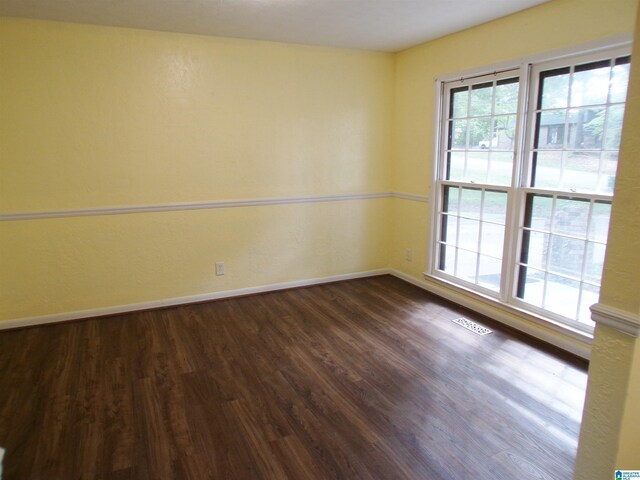 spare room featuring dark wood-type flooring, visible vents, and baseboards