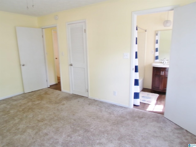 unfurnished bedroom with ensuite bathroom, a closet, a sink, and carpet floors