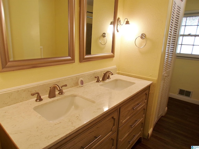 bathroom featuring wood finished floors, double vanity, a sink, and visible vents