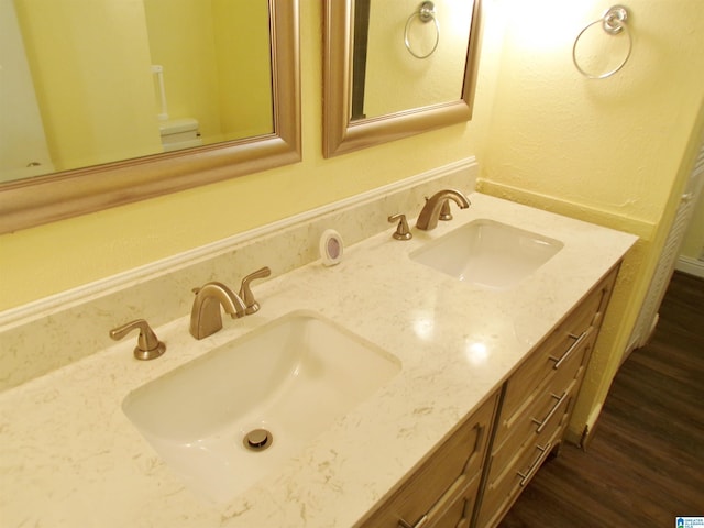 full bath with a sink, toilet, double vanity, and wood finished floors