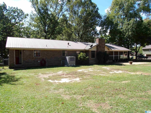 back of house with a yard, metal roof, brick siding, a chimney, and central AC unit