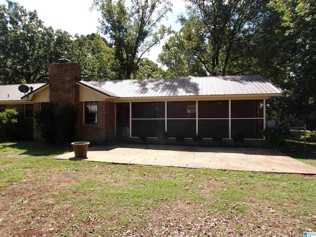 back of house featuring a sunroom, a patio area, metal roof, a lawn, and brick siding