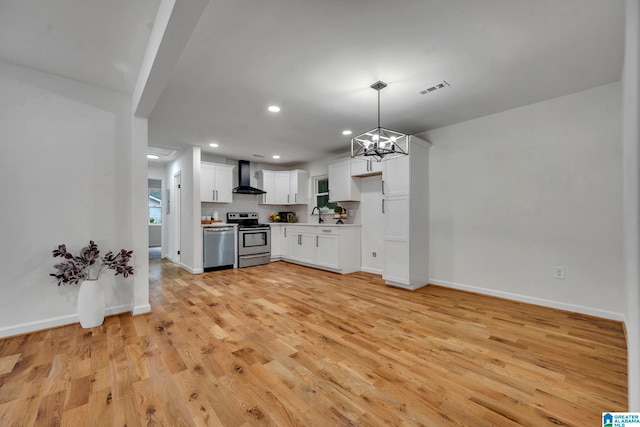 kitchen featuring pendant lighting, white cabinetry, wall chimney exhaust hood, an inviting chandelier, and appliances with stainless steel finishes