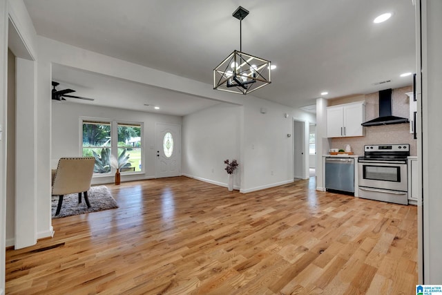 kitchen with light wood-type flooring, white cabinets, wall chimney range hood, backsplash, and appliances with stainless steel finishes