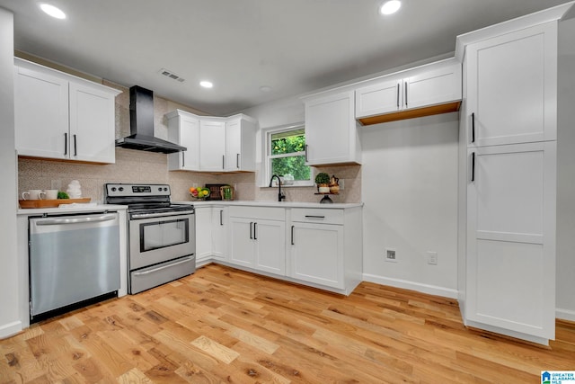 kitchen featuring light hardwood / wood-style floors, tasteful backsplash, white cabinets, wall chimney exhaust hood, and stainless steel appliances