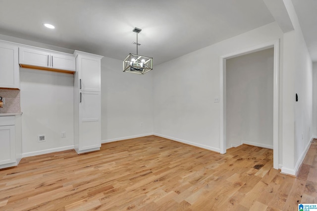 unfurnished dining area with an inviting chandelier and light wood-type flooring