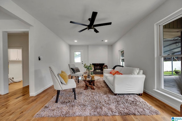 living room with light wood-type flooring, ceiling fan, and a fireplace